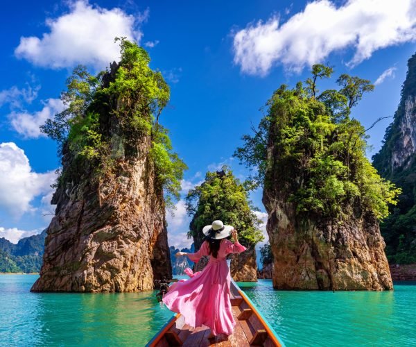 Beautiful girl standing on the boat and looking to mountains in Ratchaprapha Dam at Khao Sok National Park, Surat Thani Province, Thailand.