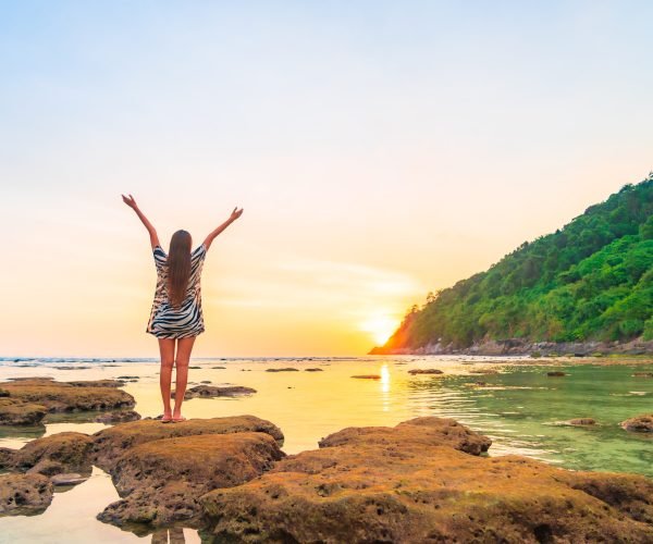 Portrait asian woman stand on the rock at sunset around beach sea ocean in travel vacation trip